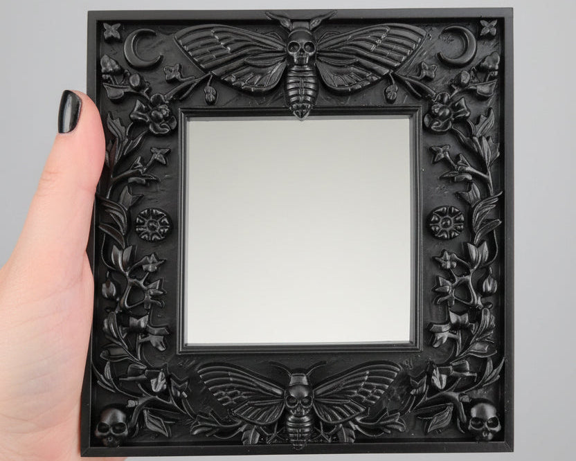 Dark gothic Death’s Head Moth light switch surround mounted on wall, ornate black home décor cover for UK light switches.